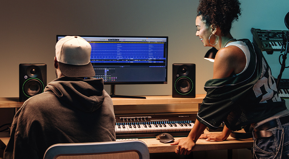 Dos personas trabajando en un home studio con monitores Mackie CR y un teclado MIDI frente al ordenador