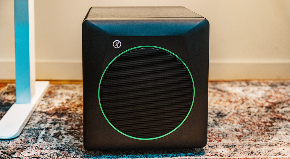 Subwoofer de estudio Mackie CR8SBT con su anillo verde caracteristico, colocado en el suelo junto a una mesa