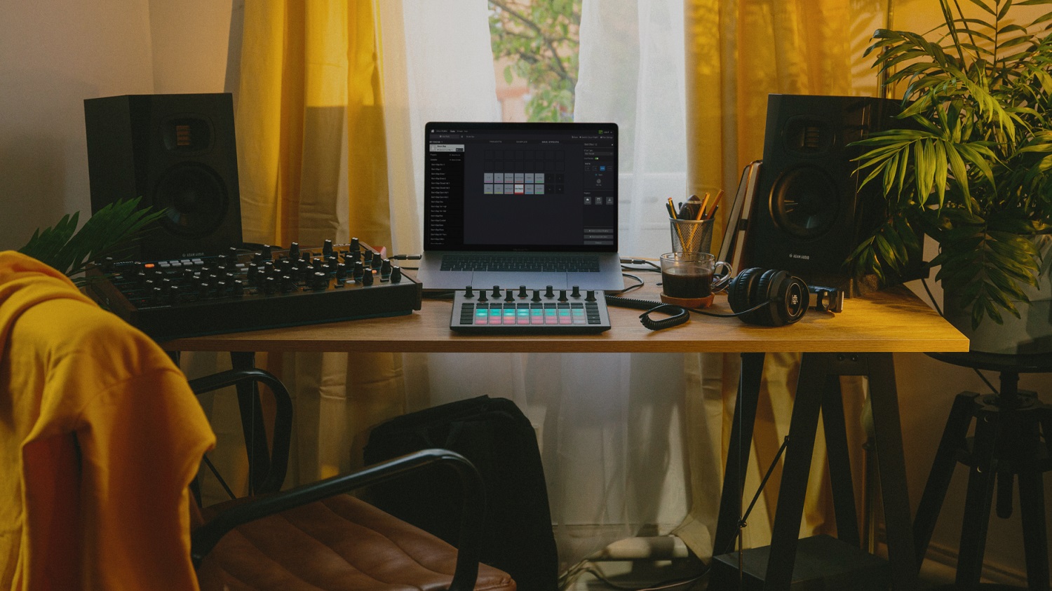Pareja de ADAM T5V en un escritorio de producción con portátil, controlador de pads, sintetizador y auriculares