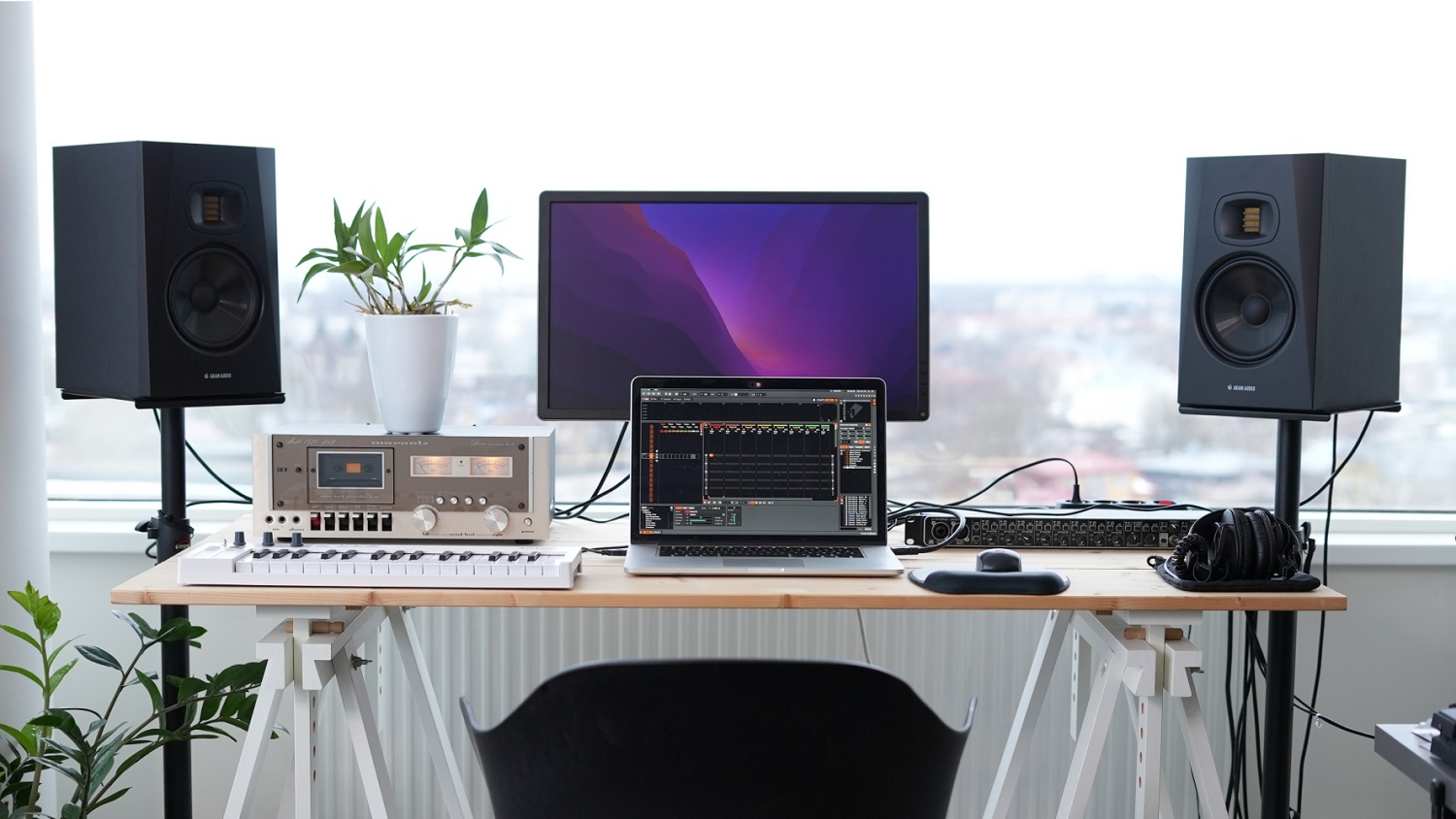 Pareja de ADAM T7V sobre pies de suelo a ambos lados de un escritorio con pantalla, portátil, teclado MIDI e interfaz de audio