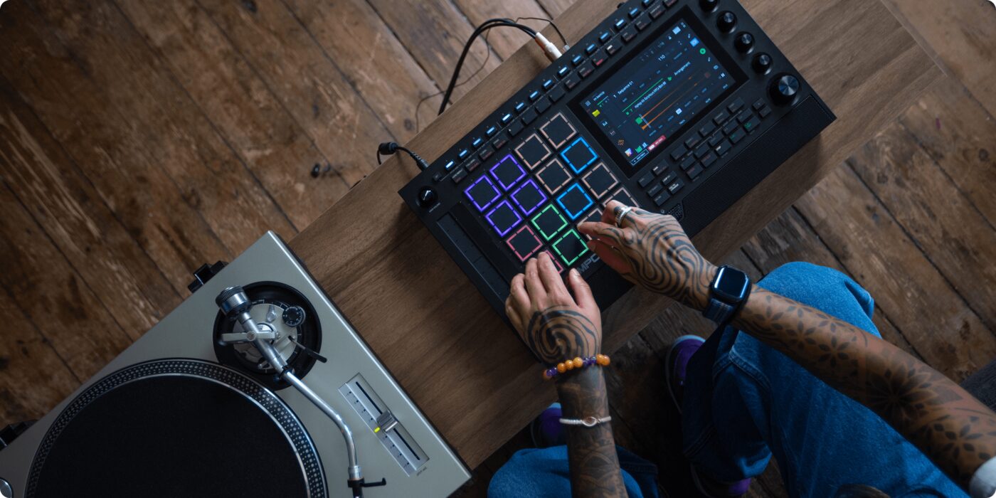 Vista cenital de unas manos sobre la MPC Live III junto a un plato giradiscos