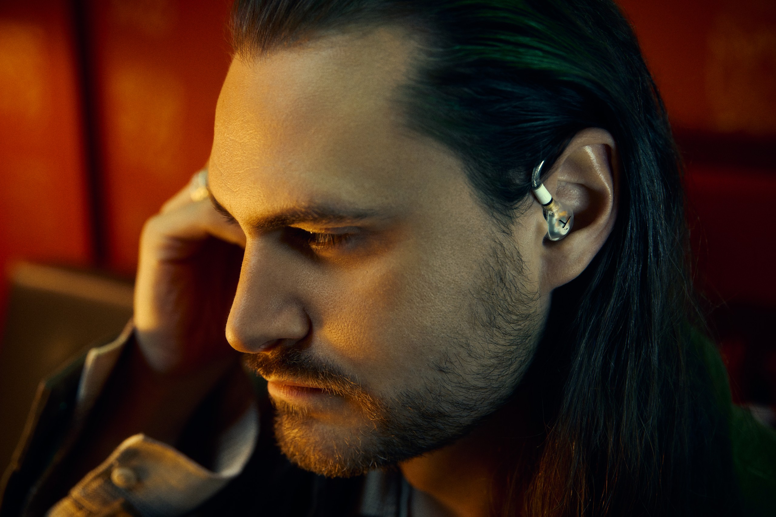 Músico de cabelo comprido a ajustar um Beyerdynamic DT 30 IE no ouvido, num ambiente de luz quente