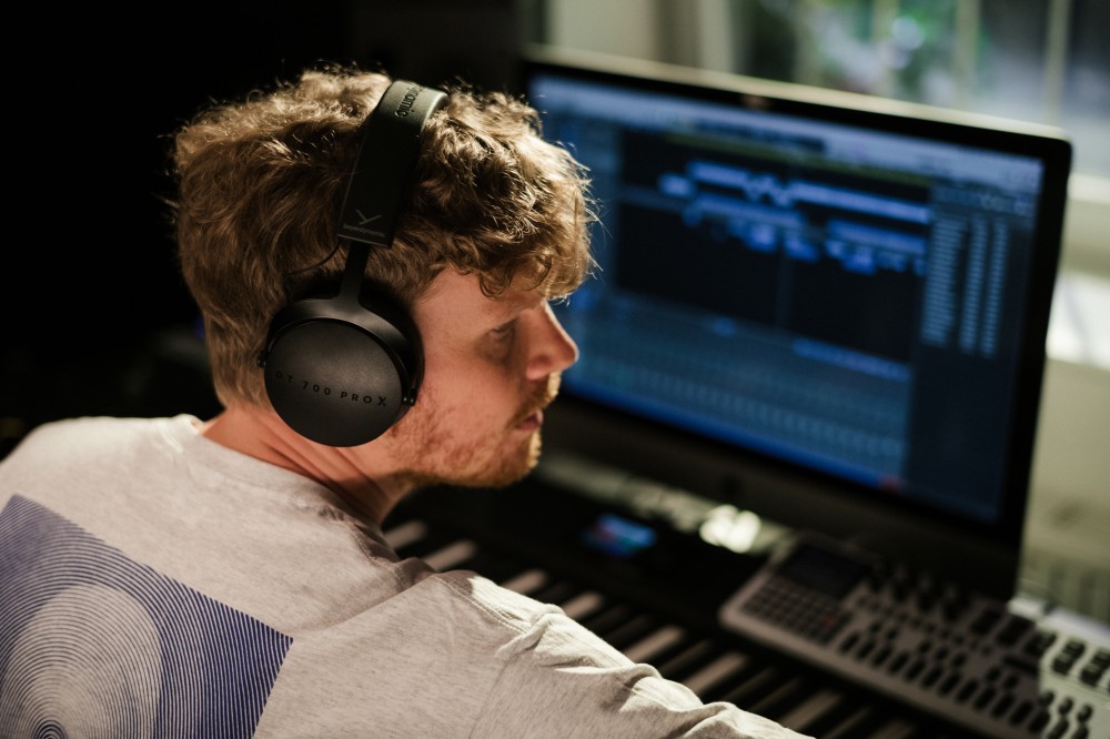 Produtor a trabalhar em frente ao computador e ao teclado com os Beyerdynamic DT 700 PRO X colocados