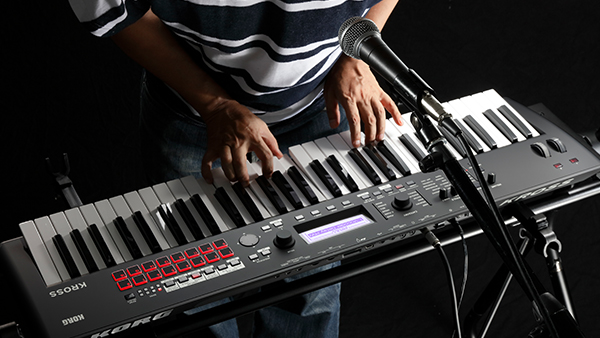 Músico a cantar com um microfone ligado ao Korg KROSS 2 enquanto toca