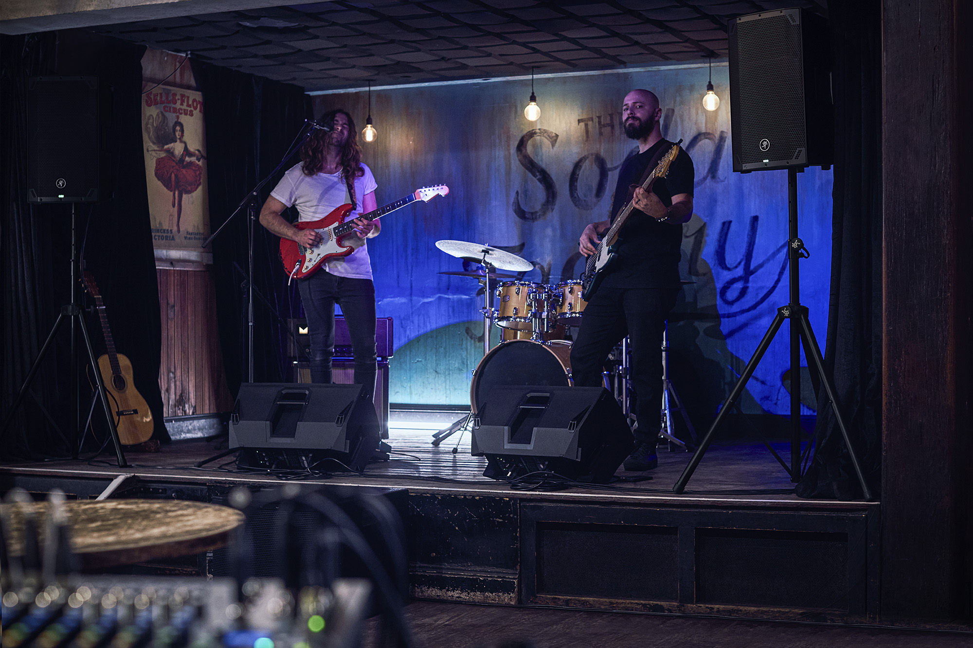 Banda tocando en un club con altavoces Mackie Thump15v4 sobre trípode y monitores de cuña en el escenario