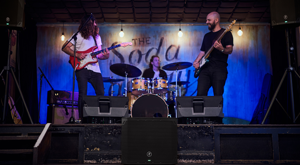 Banda en directo en un club con un subwoofer Mackie Thump18Sv4 en el suelo delante del escenario